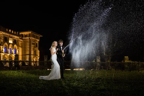 Hochzeitspaar öffnet Champagner bei Nacht vor beleuchtetem Schloss