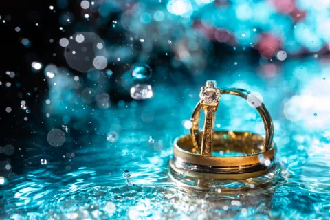 Zwei Eheringe in türkisblauem Wasser, umgeben von schwebenden Tropfen