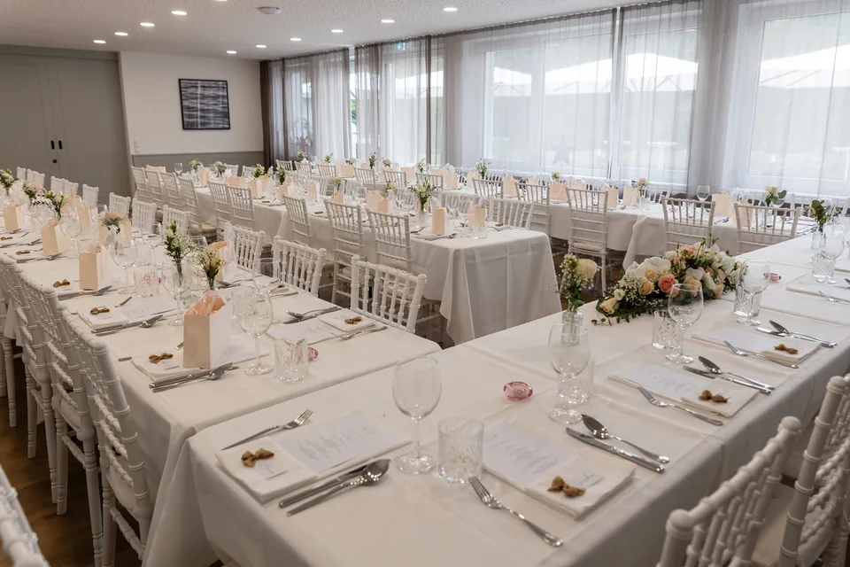 Festsaal im Das Haidensee mit langen weiß gedeckten Tafeln, weißen Stühlen und Blumen in Glasvasen