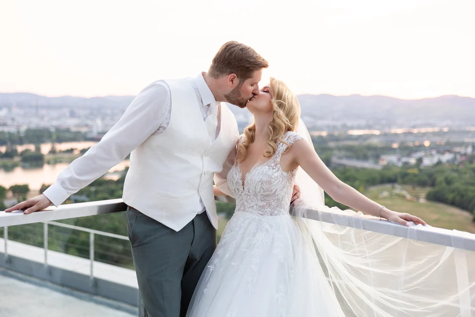 Hochzeitspaar küsst sich bei Sonnenuntergang auf einer Dachterrasse hoch über Wien