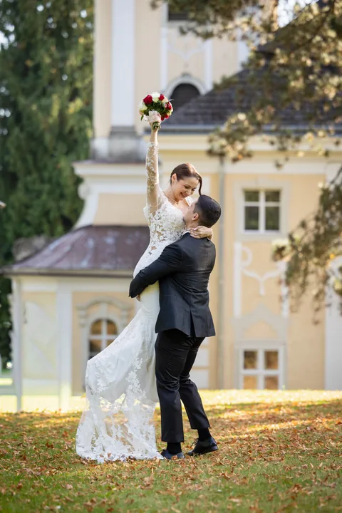 Bride raising her bouquet in celebration in front of a yellow palace facade