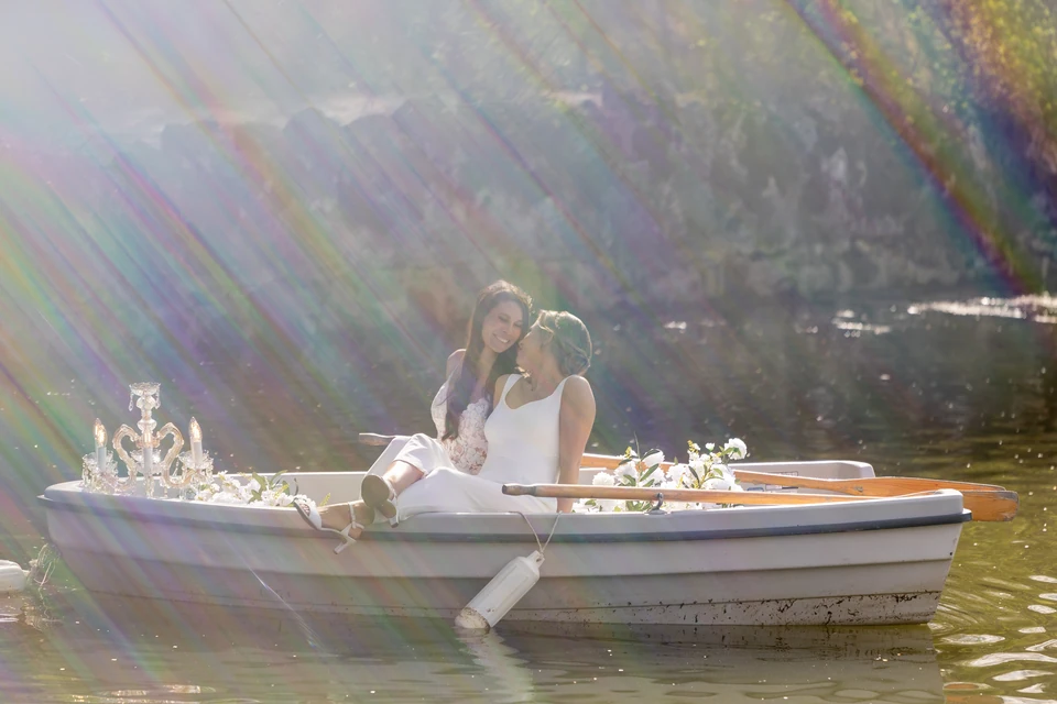 Zwei Bräute sitzen mit Kronleuchter und Blumen im Ruderboot auf dem Teich von Schloss Hernstein