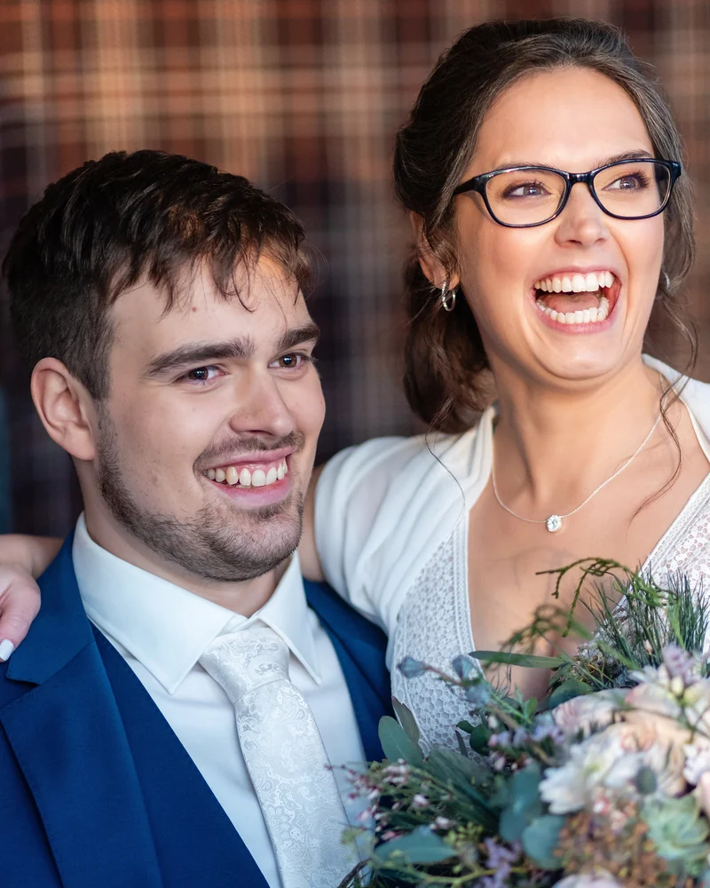 Lachendes Hochzeitspaar mit winterlichem Brautstrauß aus Eukalyptus und Kiefer