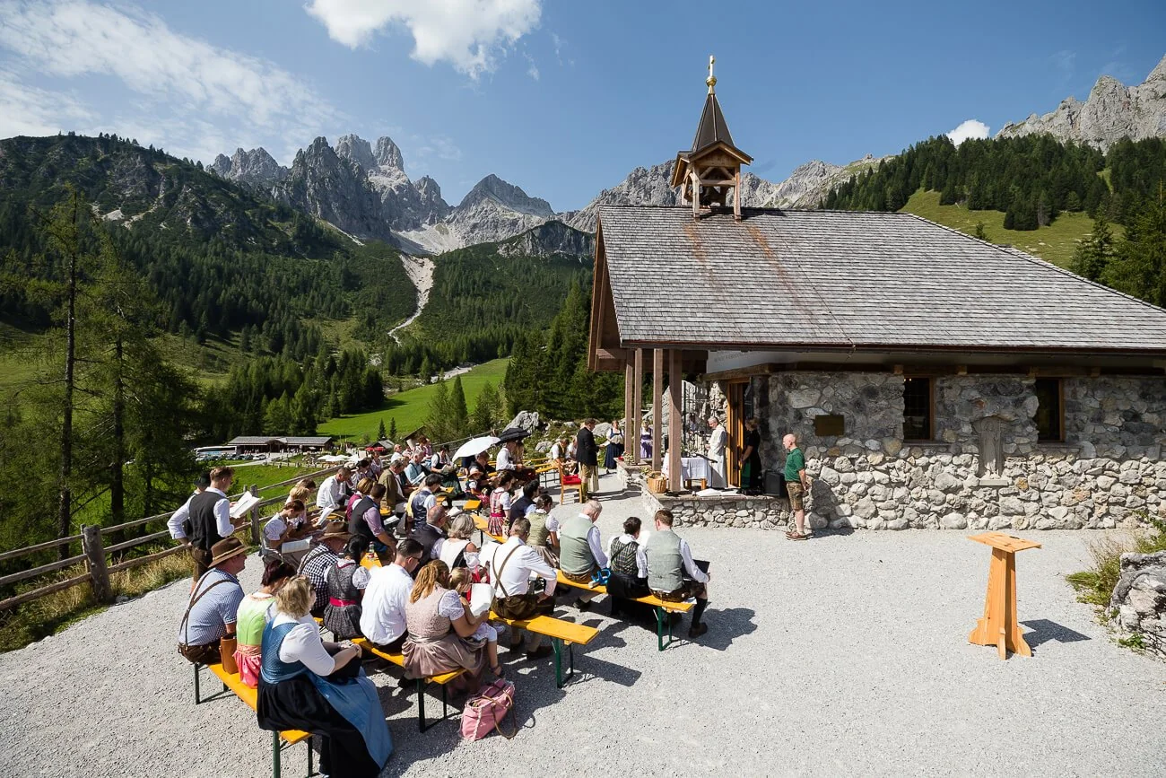 Hochzeitsgesellschaft vor einer Kapelle auf der Alm mit Bergpanorama in Österreich