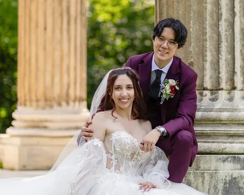 Wedding couple by historic columns in Laxenburg palace park, the groom in a burgundy suit