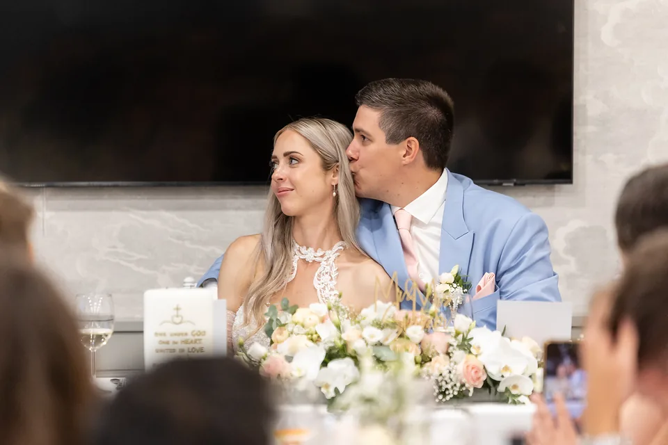 Das Hochzeitspaar an der Tafel im Festsaal von Das Haidensee, im Vordergrund Blumen und Gäste
