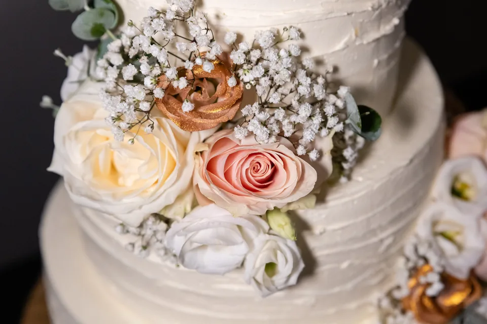 Detail der Hochzeitstorte mit rosa Rosen, Schleierkraut und kupferfarbenen Blüten