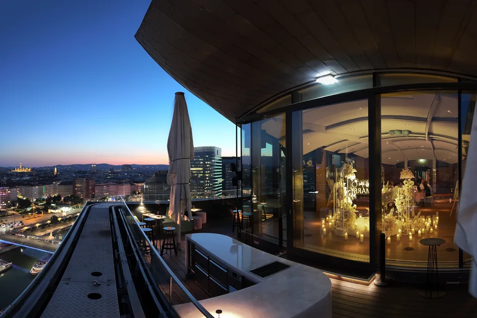 The rooftop terrace of Juwel Vienna at dusk, the lit city behind