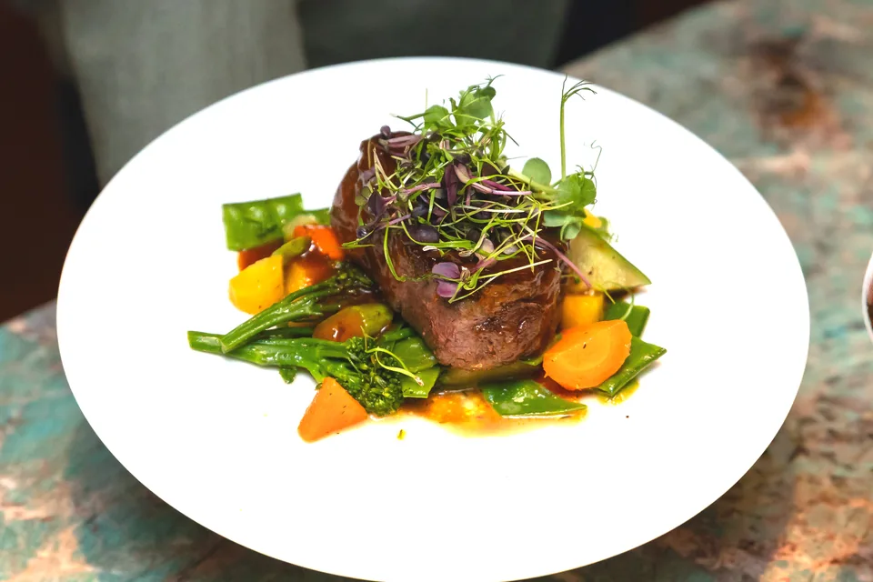 Beef fillet with vegetables on a white plate, a glass of red wine beside it