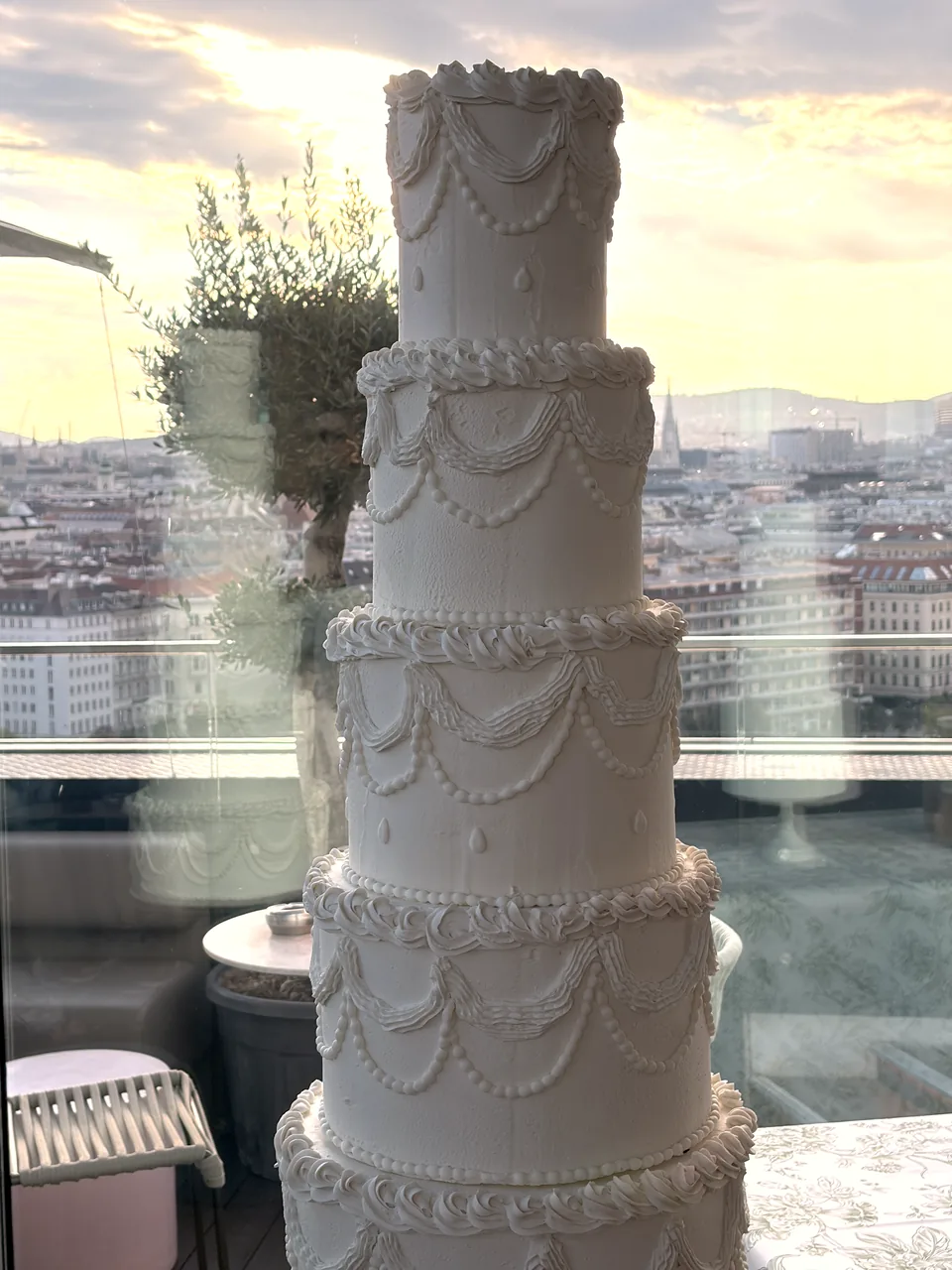 Multi-tier white wedding cake in front of the window front of Juwel Vienna, the city behind in evening light