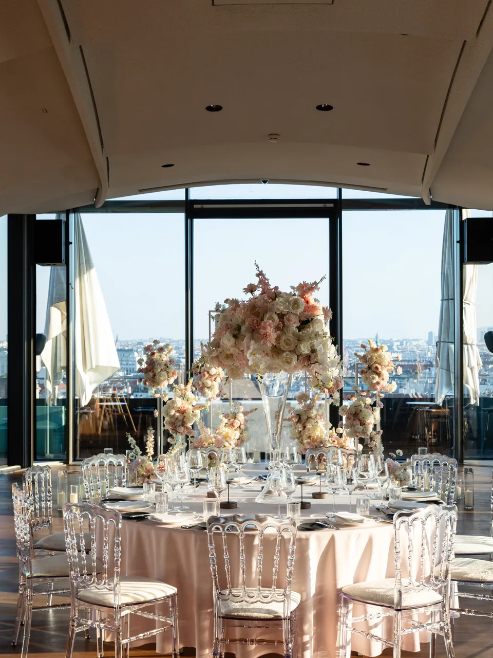 Round wedding table with a tall floral centerpiece in front of the full height window front on the fifteenth floor of Juwel Vienna