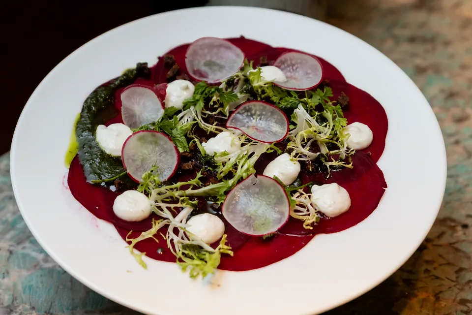 Beetroot carpaccio with radishes and herbs on a white plate