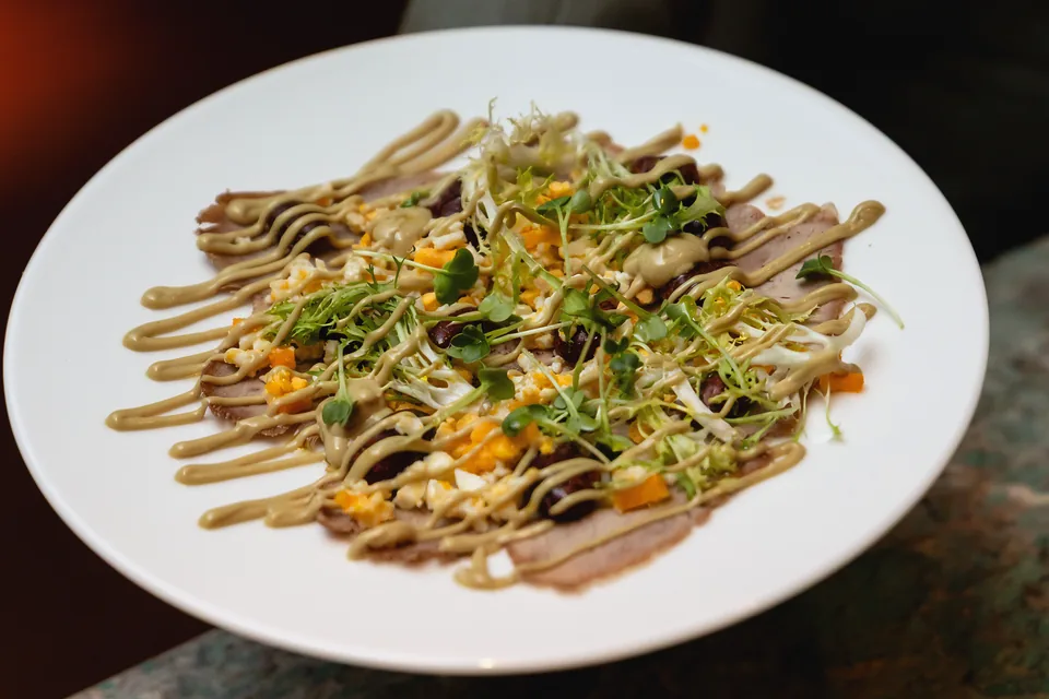 Tafelspitz carpaccio with pumpkin seed mayonnaise and sprouts on a white plate
