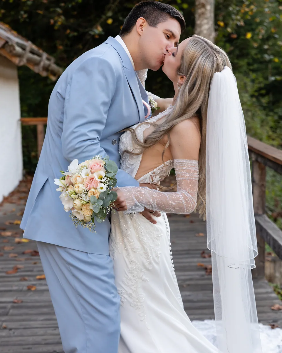 Hochzeitspaar küsst sich auf dem Holzsteg, der Schleier fällt über das Geländer