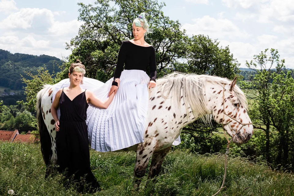Same-sex wedding couple in the paddock with a horse