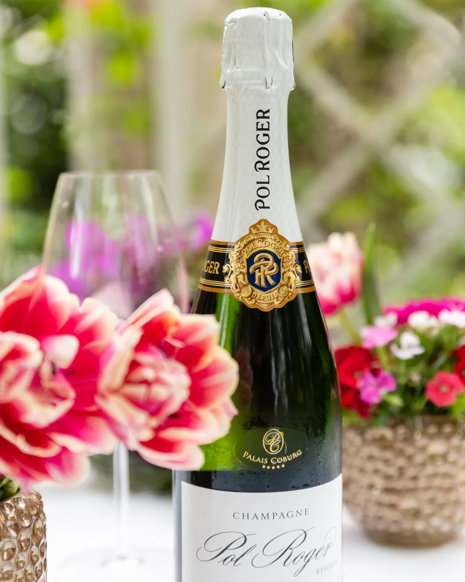 Flasche Pol Roger zwischen roten und rosa Blumen im Garten des Palais Coburg
