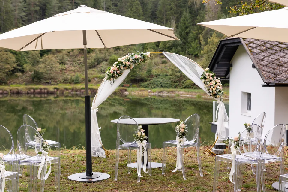 Vorbereitete freie Trauung am Haidensee: Blumenbogen, transparente Stühle und Sonnenschirme am Ufer