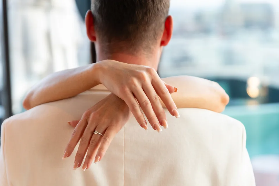 Newly engaged woman embracing her partner from behind, her hands with the engagement ring resting on his shoulder
