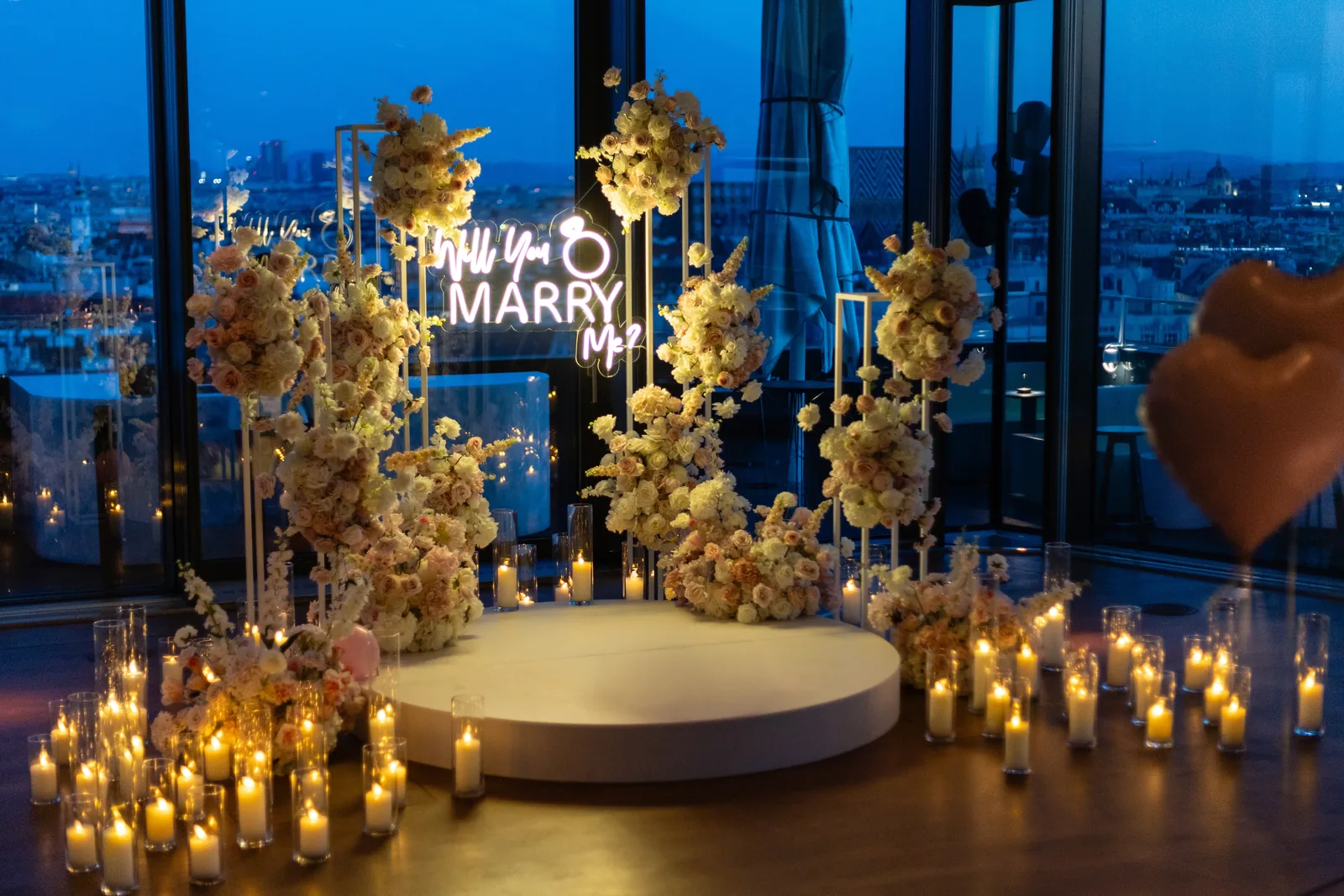Proposal setup with roses, candles and a Will You Marry Me sign above the rooftops of Vienna at blue hour