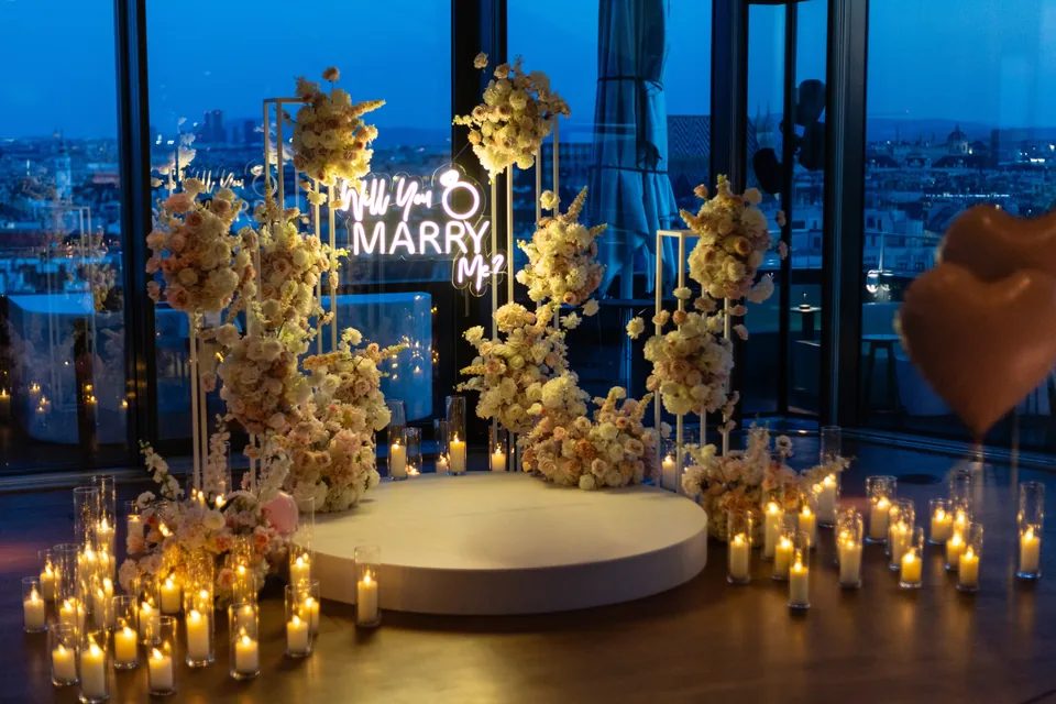 Floral arch with candles and a will-you-marry-me neon sign at blue hour at Juwel Vienna, the lit city behind