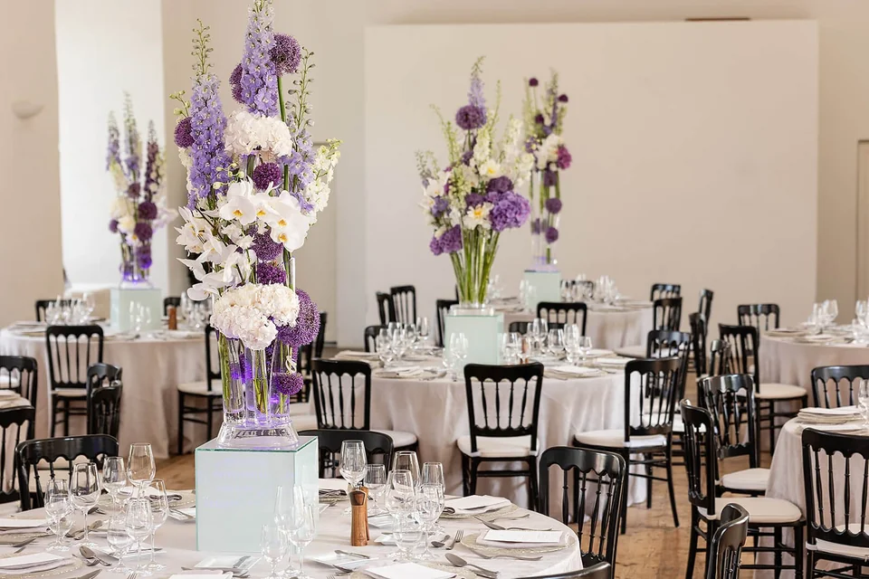 Festlich gedeckte Tische mit violettem Blumenschmuck im Säulenraum von Schloss Walpersdorf