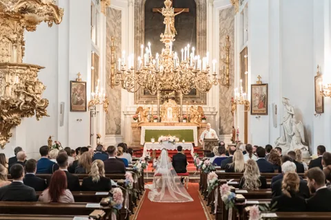 Kirchliche Trauung mit goldenem Kerzenluster, Blick über die Gäste zum Altar